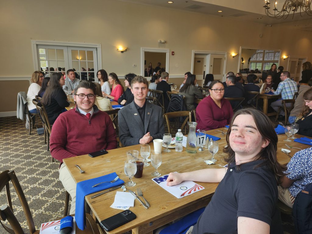 Three high school boys sit at a table, all looking at the camera smiling.