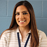 A woman with long dark hair, wearing a light striped shirt. She is smiling.