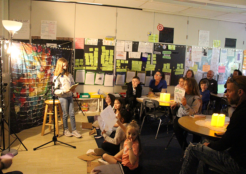 People watch as a fourth-grade students sits on a stool reading poetry.