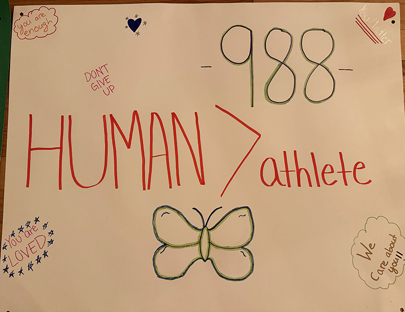 A poster handwritten that says 988. Human > athlete. Don't give up. You are loved. We care about you. You are enough