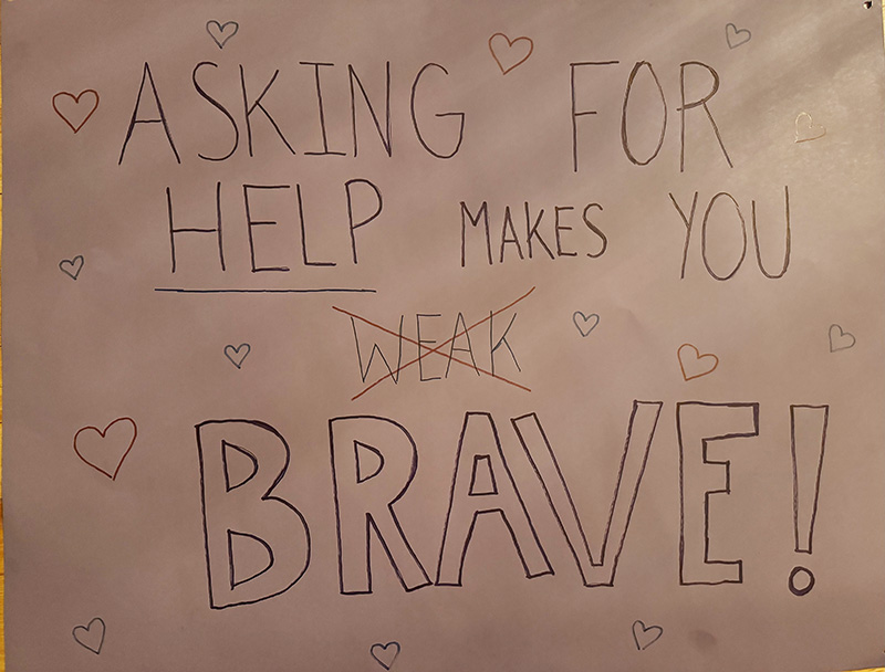 A poster that says Asking for help makes you Brave. The word weak is crossed out.