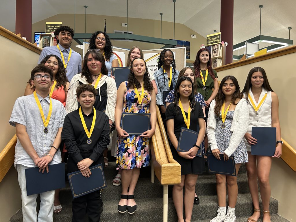 A group of 15 high school students stand on steps. They all have a gold medallion around their necks.