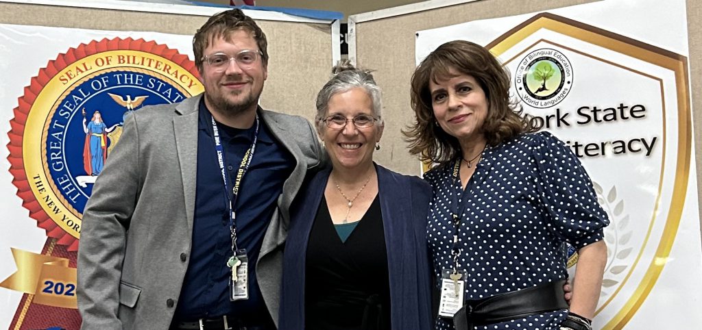 Three adults, a man on the left and two women, stand together smiling.