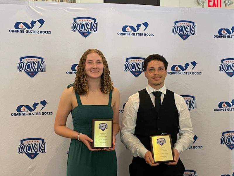 Two high school seniors, a young woman on the left and young man on the right, stand next to each other holding plaques.