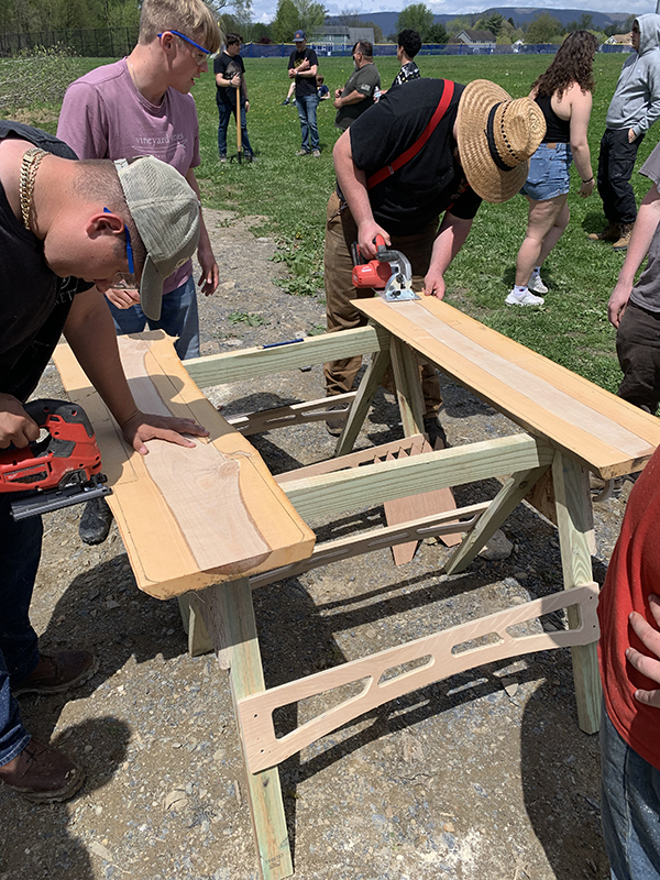 Students use hand saws to cut  a wood plank.
