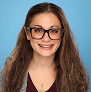 A woman with long dark hair and glasses smiles.