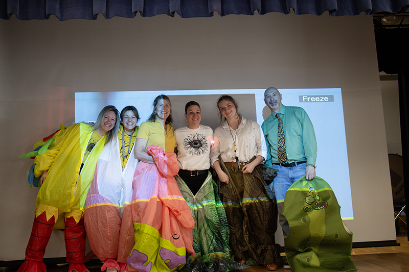 Six people stand together smiling. They are wearing blow-up costumes but the costumes are zipped down so you can see who was waring them.