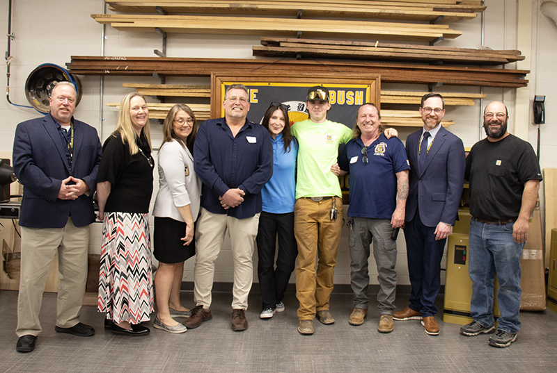 A group of nine people stand in a row, with a high school student in the center.
