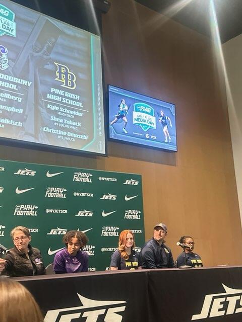 Five people sitting on a stage, doing a press conference.