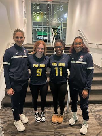 Two high school girls in the center wearing their football jerseys that say Pine Bush, flanked by two women wearing athletic wear.