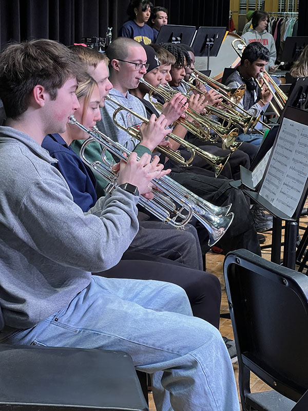 High school students sit in a row playing horns.