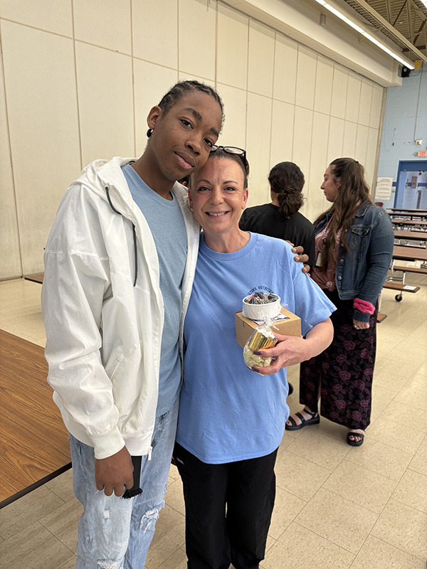 A middle school student in a blue shirt and white jacket hugs an adult. They are both smiling.