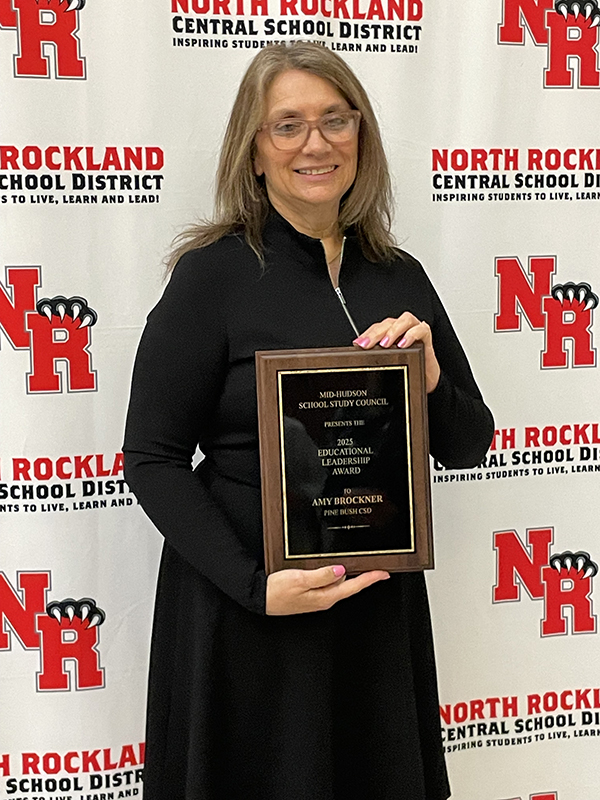 A woman in a black dress smiles and holds an award.
