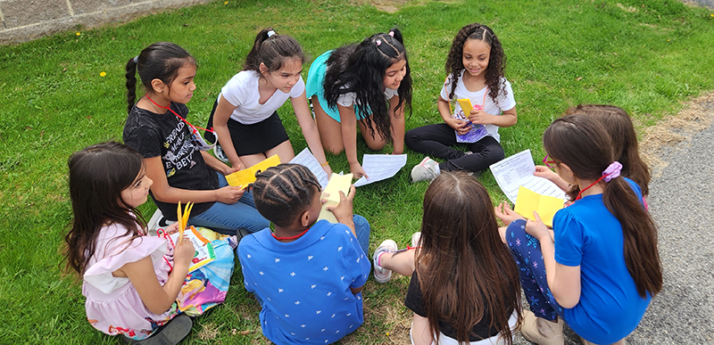 A group of eight elementary age girls sit in a circle sharing poems with each other.