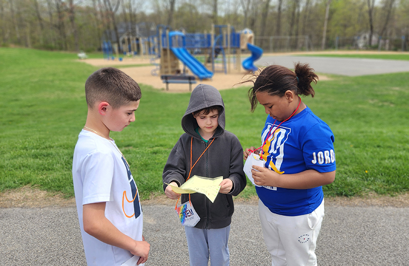 Three elementary students stand together sharing their poems with each other.