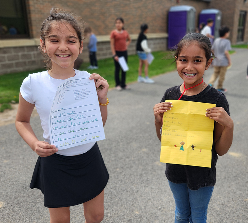 Two girls hold up their poems and smile.