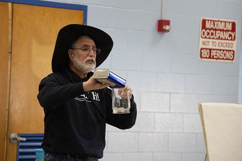 a man wearing black and a black wizard hat pours a solution into a beaker.