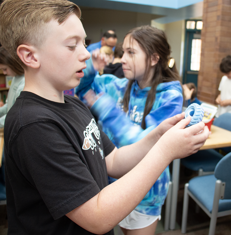 A fifth-grade boy with short blonde hair, holds a plastic fidgit in his hands and looks at it.
