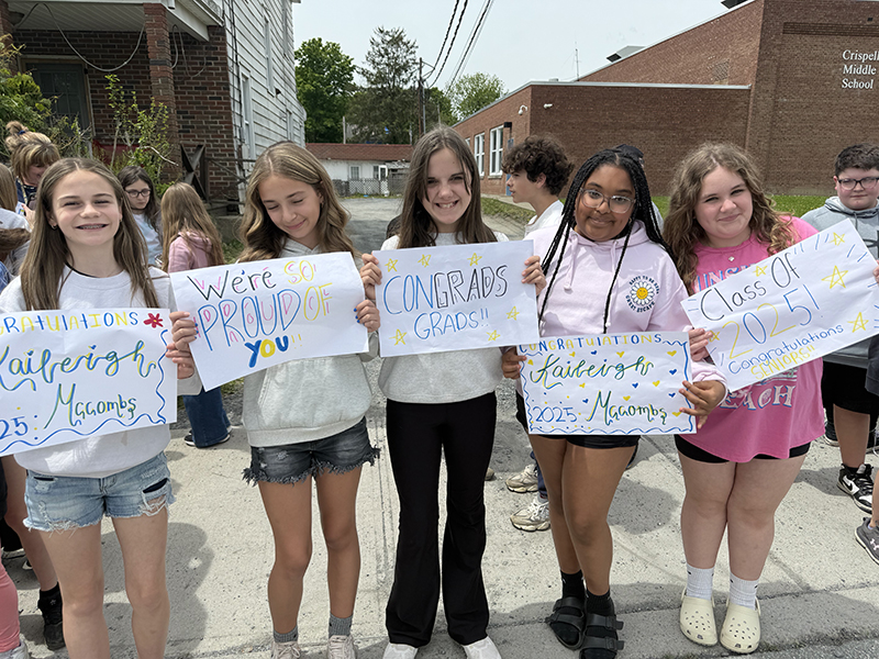 A group of middle school girls hold up supportive signs for graduates.