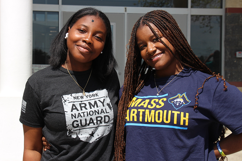 Two high school girls smile wearing their college and army national guard shirts.