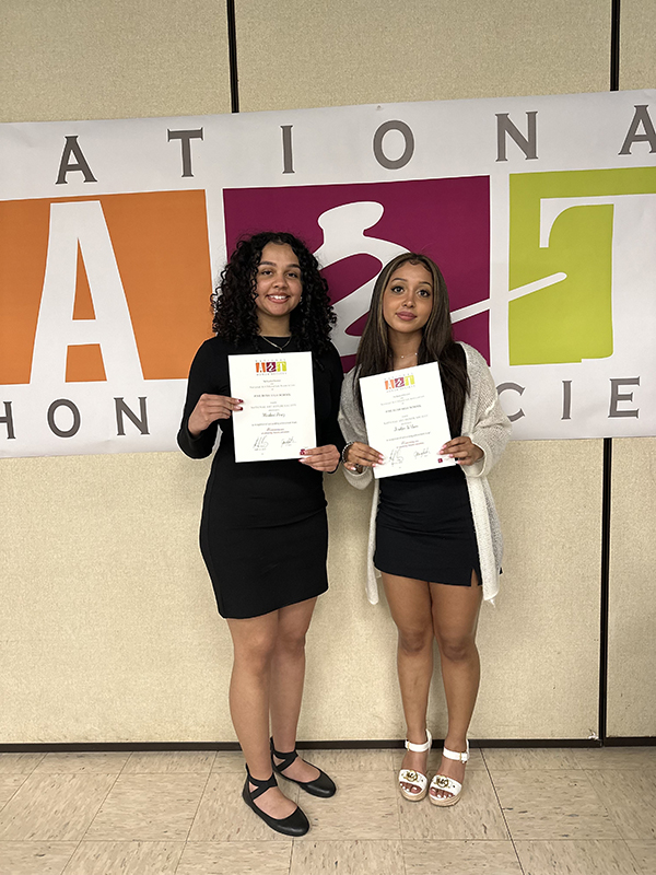Two high school students stand holding certificates in front of them.