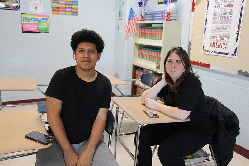 Two high school students sit at desks.