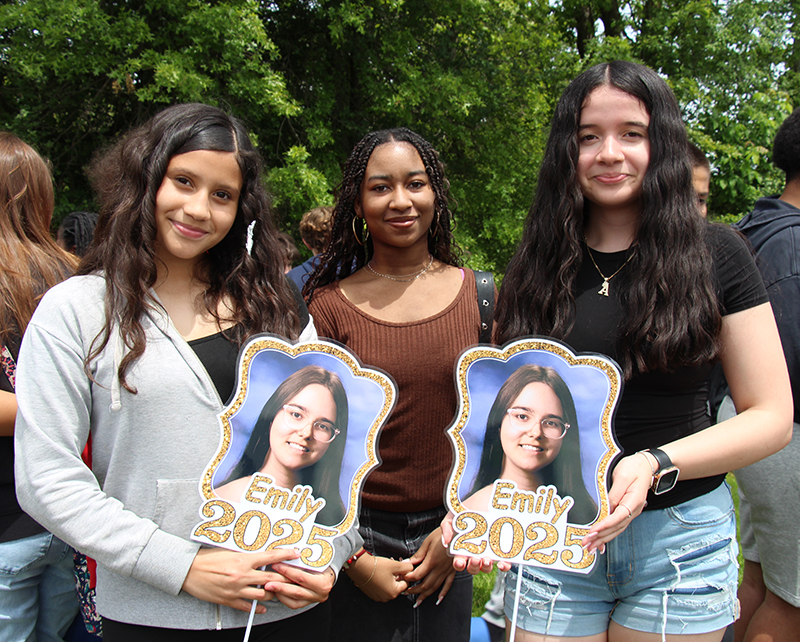 Three middle school girls hold signs that have a picture of a high school senior on them.