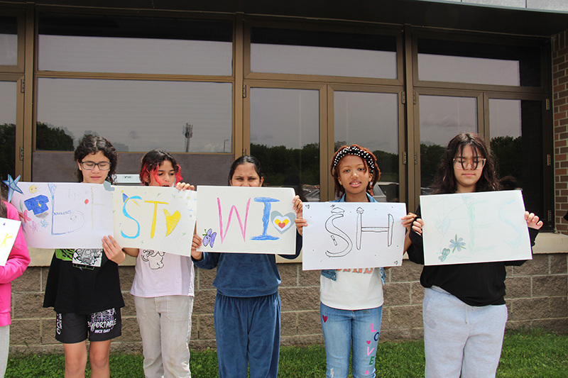 Five elementary kids hold up signs that when put together say Best wishes!