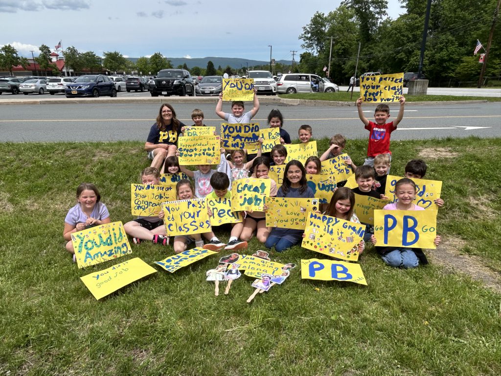 A group of younger elementary school students hold yellow and blue signs with positive messages for the grduates.