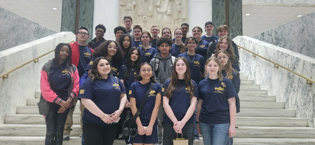 Twenty-five high school students stand on a marble staircase.