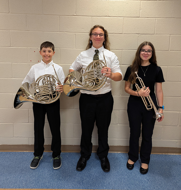 Three middle school age students stand holding their musical instruments. Two are wearing white shirts and ties and the other is wearing all black.