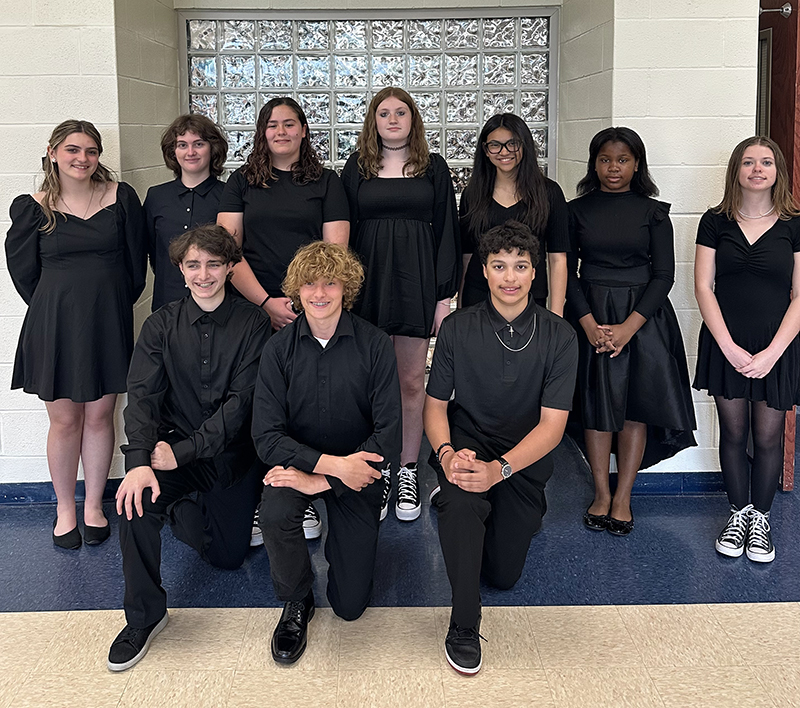 A group of 10 middle school age students sit in two rows. They are all dressed in black.