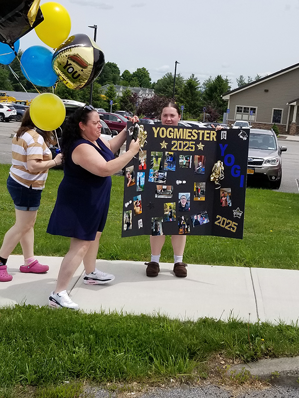 Adults hold up a large sign with lots of pictures on it.