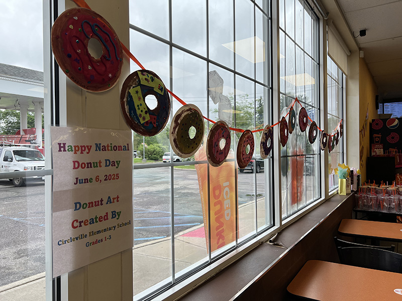 A string of artwork that looks like donuts hangs along a window at a donut shop.