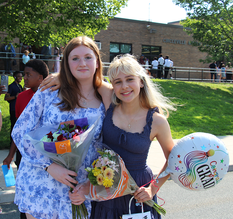 Two eighth-grade girls dressed nicely, one holding flowers and a balloon, smile.