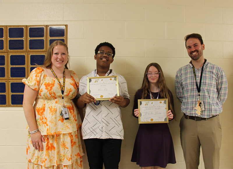 A woman on the left and a man on the right flank a young man and young woman who are holding up certificates.