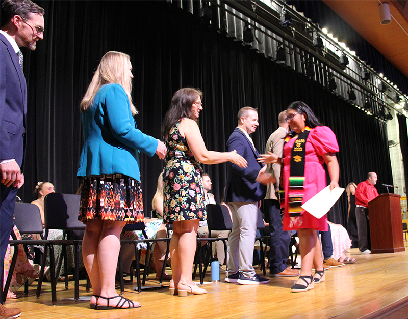 An eighth-grade girl shakes hands with a line of adults on a stage. 