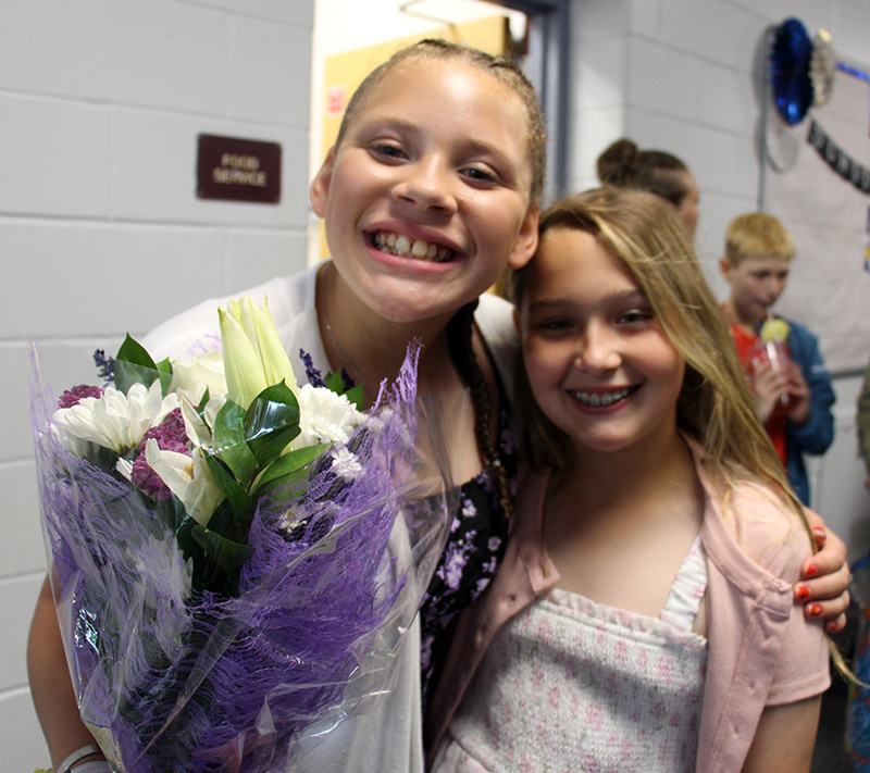 Two fifth-grade girls stand together with big smiles.
