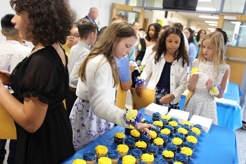 Fifth-grade girl pick up cupcakes from a blue tableclothed table.