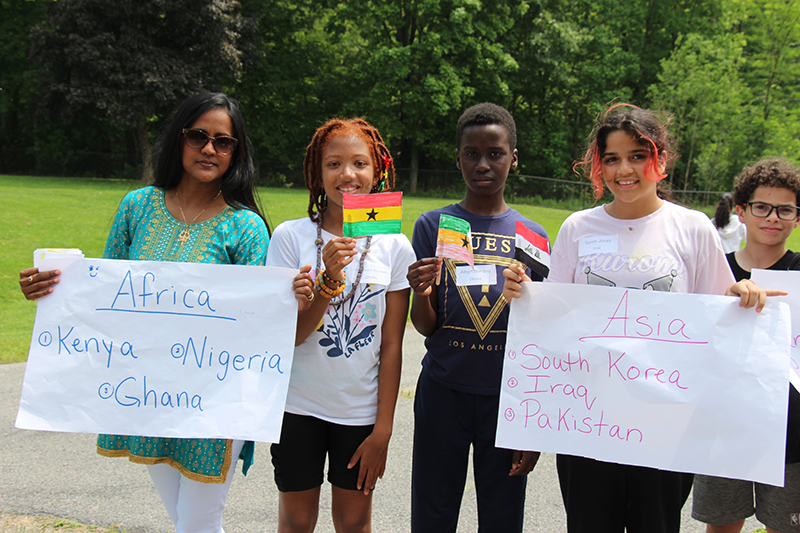 A woman and four elementary students stand together, holding different flags and signs for their parade.