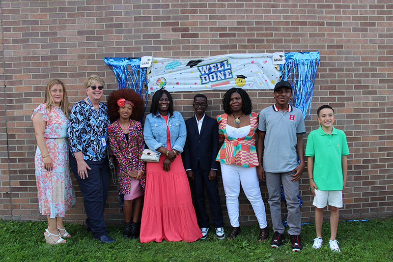 A group of eight people, including five adults and three fifth-grade kids, stand under a banner that says Well done!