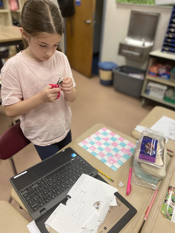 A fourth-grade girl cuts out little chess pieces from paper.