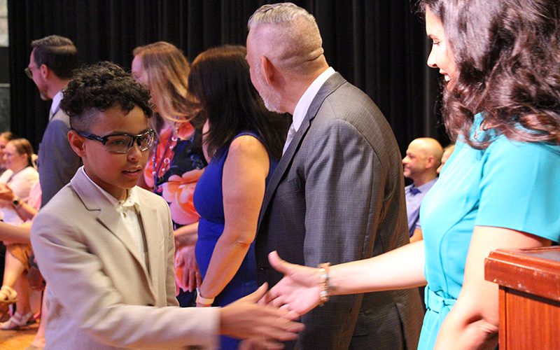 A fifth-grade student shakes hands with a line of adults.
