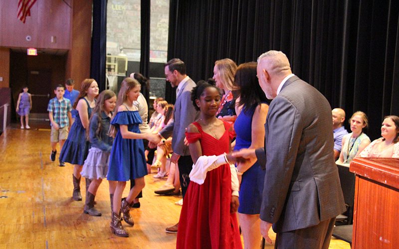 Several fifth-grade students shake hands with adults on a stage.
