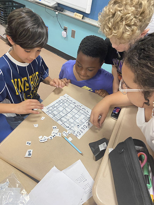 Four fourth-grade students play chess on a paper board.