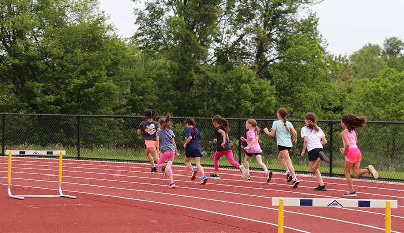 A group of eight girls run around a clay track.