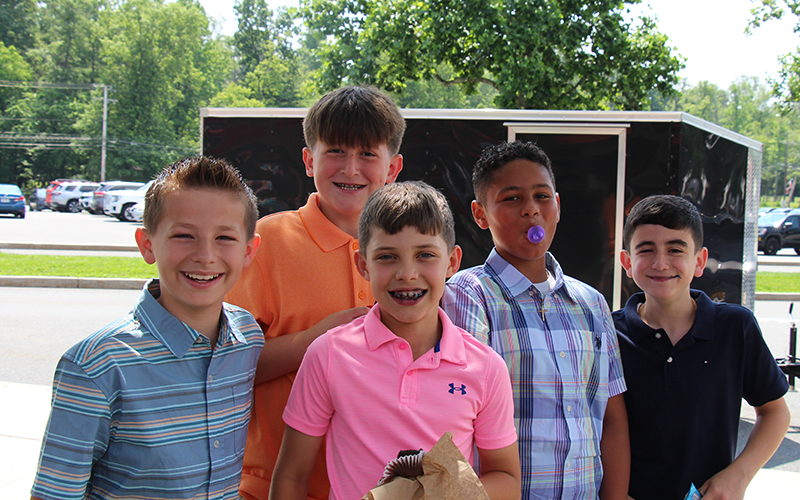 A group of five fifth-grade boys stand outside smiling. Some have cupcakes.