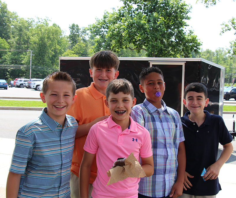 A group of five fifth-grade boys stand outside smiling. Some have cupcakes.