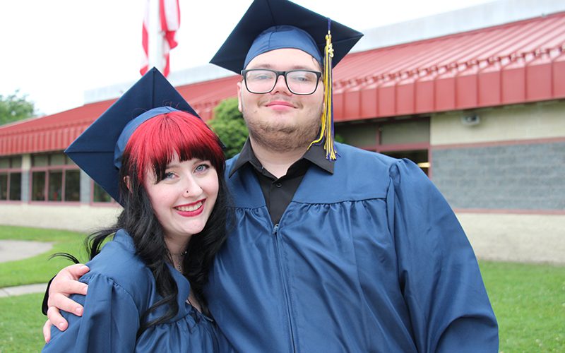Two high school seniors dressed in blue cap and gown. They are smiling.