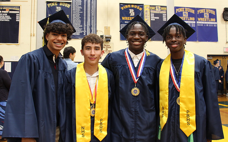 Four young men, all in blue caps and gowns, smile.